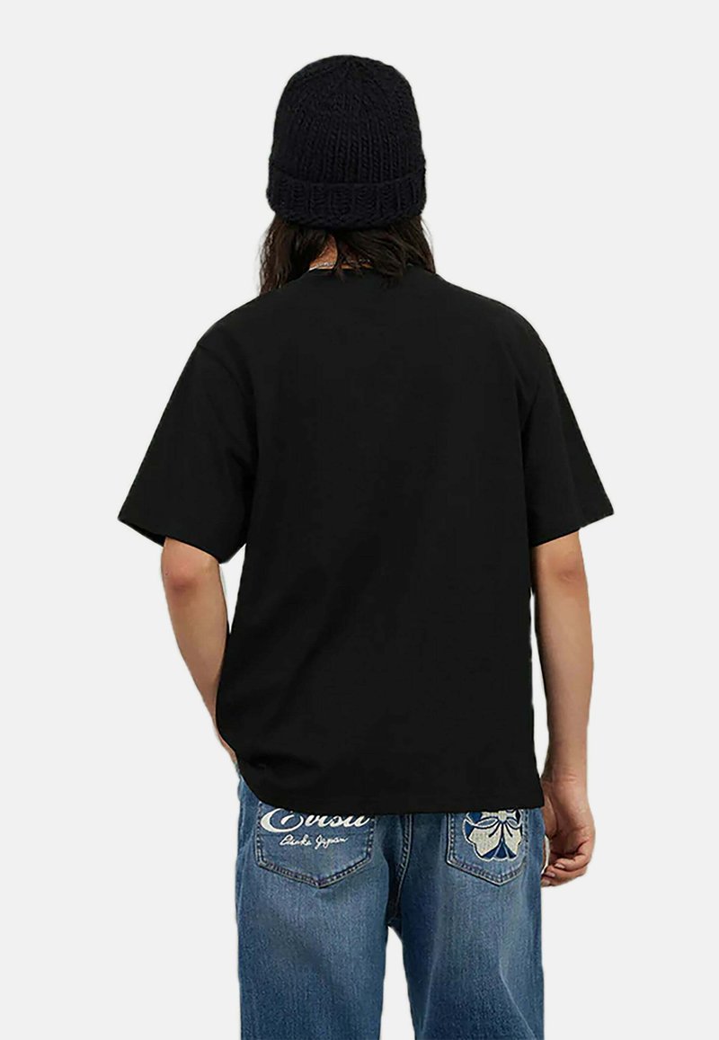Sort bomulds t-shirt med korte ærmer og en afslappet pasform. Modellen har denim jeans på med broderede blomsterdetaljer samt en sort strikket hue.