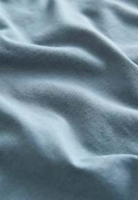 Ljust blått tyg med en mjuk, slät textur som visar subtila veck och ett finstickat mönster, vilket antyder ett bekvämt och luftigt material.