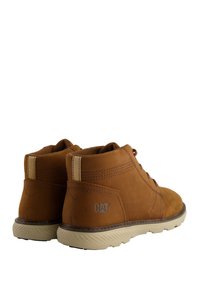 Botas de cuero marrón hasta el tobillo con un acabado texturizado, suela beige y costuras claras en contraste. Logo en el lado exterior. Diseño con cordones.