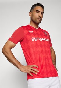 Červený futbalový dres s diamantovým vzorom, krátkymi rukávmi a kruhovým výstrihom. Logo na hrudi a text "ggmgastro" v bielej farbe.