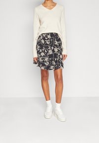 Krémový svetr s výstřihem do V v kombinaci s černou mini sukní s květinovým vzorem. K outfitu se hodí bílé tenisky a kotníkové ponožky.