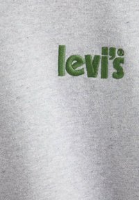 Logo "levi's" bordado en verde sobre tela gris claro, mostrando textura y detalles de costura.