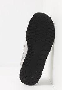 Svart gummiyttersula med djupa mönster. Ovandelen är av vitt syntetiskt material med ett meshpanel och subtil varumärkeslogga på sidan.