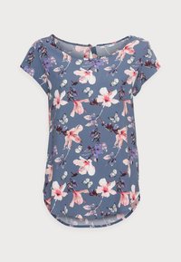 Květinová halenka z modré látky, s růžovými a fialovými květy a motýly, krátkými rukávy a zaobleným okrajem. Zapínání na knoflíky vzadu.