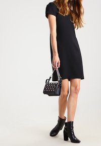 Robe noire à manches courtes avec une coupe droite. Sac à main noir avec des clous argentés et une bandoulière en chaîne. Bottines noires à talon épais.