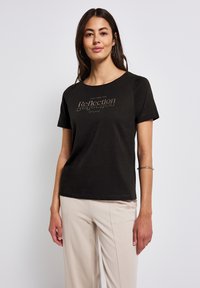 T-shirt en coton noir à manches courtes et col rond, avec un graphisme en relief doré "Prenez le temps de réfléchir" sur le devant.