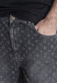 Jeans de denim negros con un sutil patrón de logotipos en toda la prenda, un acabado desgastado y un diseño clásico de cinco bolsillos con cierre de botón en la parte delantera.