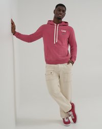 Felpa rosa con cappuccio, dotata di lacci bianchi e tasca frontale, abbinata a pantaloni cargo crema con tasche laterali e sneakers rosse.