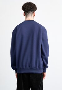 Sudadera azul marino con cuello y puños acanalados, presenta una textura suave y un corte relajado. La vista trasera muestra un color sólido y un detalle mínimo.