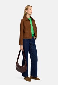 Brązowa skórzana kurtka z kołnierzykiem, zielony sweter pod spodem, niebieskie szerokie dżinsy oraz bordowa torebka na ramię. Brązowe buty dopełniają stylizację.