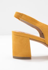 Scarpa con tacco a blocco in suede giallo, con punta aperta e design slingback. Il tacco è testurizzato e stabile, contribuendo alla sua forma strutturata.