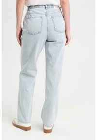Jeans à jambes larges rayés bleu clair avec une taille haute, dotés de deux poches arrière et d'un tissu doux et texturé. Portés avec des baskets blanches.