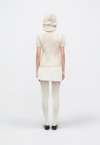 Top tricotat de culoare crem cu glugă, mâneci scurte și tiv evazat. Asortat cu colanți deschiși la culoare și pantofi negri. Textură moale și design stratificat.