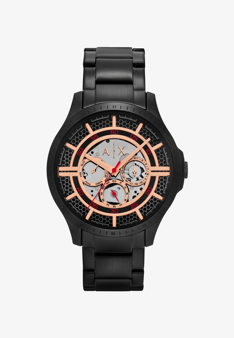 Montre-bracelet en métal noir avec des index couleur or rose, trois sous-cadrans pour le jour, la date, l’heure 24h, et une trotteuse rouge sur cadran nid d’abeille.