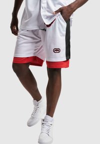 Witte sportshorts met rode accenten, zwarte zijpanelen, verstelbare tailleband en zijzakken. Draagt met witte hoge sneakers.
