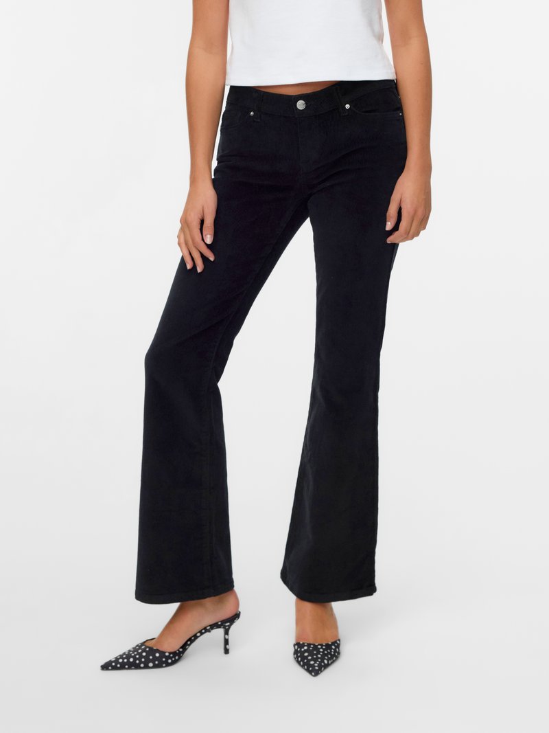 Jean flare en velours côtelé noir avec poches avant, taille ajustée et texture lisse, associés à des talons hauts à pois.