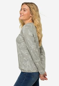 Szara koszula z długim rękawem w białe wzory żaglówek, miękka w dotyku, luźny krój i zaokrąglony dekolt. Połączona z niebieskimi dżinsami.