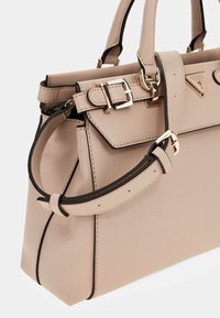 Vaaleanbeige nahkainen käsilaukku, jossa on jämäkkä muoto, kultaiset varusteet, säädettävä hihna ja kontrastiväriset yksityiskohdat.