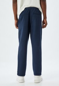 Mørkeblå sweatpants med elastisk talje, synlige sidelommer og ribbenede ankler, lavet af blødt bomuldsmateriale.