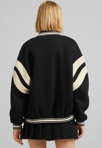 Übergroßer schwarzer Pullover mit cremefarbenen Streifen an den Ärmeln, geripptem Kragen und Bündchen, weicher Textur und elastischem Bund.