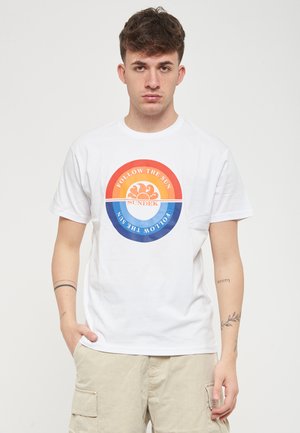 Weißes T-Shirt mit kurzen Ärmeln, das ein rundes Logo mit dem Text "FOLLOW THE SUN" in orange, gelb und blau zeigt. Angenehm glatte Stofftextur.