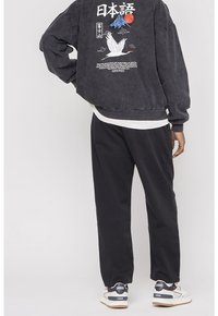 Černá manšestrová bunda s japonskými motivy na zádech, doplněná černými kalhotami a bílými teniskami s barevnými akcenty.