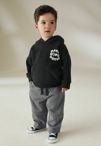 Sort hoodie med hvid tekstprint "MAKE SOME NOISE" på brystet, parret med gråstribede sweatpants og navy sneakers.