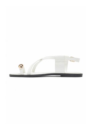 Hvid flad sandal med sort sål, med tynde stropper, en metalisk guldtå-ring og en ankelrem med spænde.