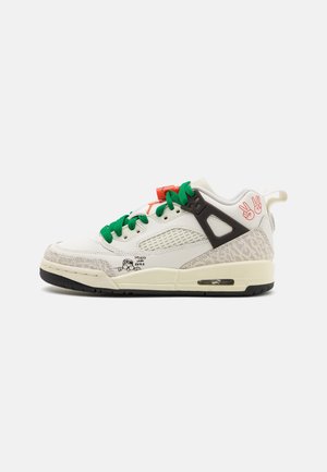 Biały i beżowy sneaker z zielonymi sznurówkami, czarnymi plastikowymi wzmocnieniami, czerwonymi symbolami dłoni pokoju oraz małym czarnym rysunkiem kreskówkowym blisko podeszwy.