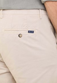 Beige katoenen broek met een achterzak met knoopsluiting en een marineblauwe label met de tekst "Faconnable." Gladde textuur, getailleerde pasvorm.