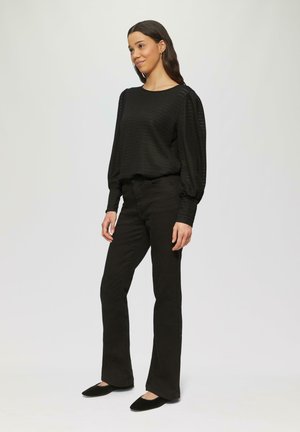 Zwarte gebreide trui met lange pofmouwen, gecombineerd met zwarte flare jeans en zwarte flats, tegen een neutrale achtergrond.