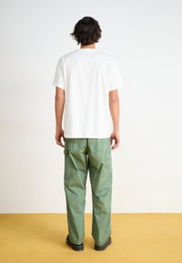 T-shirt en coton blanc à coupe décontractée, associé à un pantalon cargo vert olive avec plusieurs poches et une jambe légèrement fuselée.
