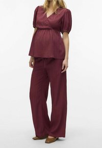 Burgundské peplum top s krátkými nabíranými rukávy a zavinovacím designem, spárované s volnými, odpovídajícími kalhotami. Hladká textura a vzor s vertikálními pruhy.