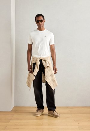 Witte short-sleeve t-shirt, beige geruite overhemd om de taille geknoopt, zwarte jeans, beige schoenen en donkere zonnebril. Glad texturen en casual stijl.