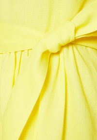 Tissu jaune doux noué en un nœud formant des plis plissés sous le nœud, mettant en valeur une texture lisse et une couleur vive.