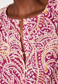 Camicia a bottone con un motivo floreale paisley nei colori rosa, arancione e bianco. Tessuto morbido con scollatura rotonda e una leggera texture.