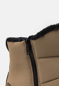 Brun dragkedja stövel med en texturerad yta, som har en kontrasterande svart fuskpälskant upptill och en YKK-dragkedja för stängning.