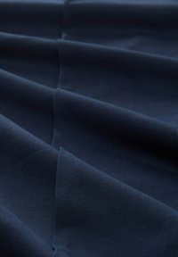 Mörk marinblått tyg med en texturerad yta, som har flera veck som skapar djup. Materialet verkar hållbart och slätt.