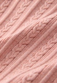 Blødt lyserødt strikstof med gentagne lodrette flettede kabelmønstre og en ribbet tekstur.