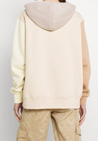 Huvtröja med färgblockdesign i beige, ljusgul och ljusbrun. Mjuk tyg med synliga sömmar och muddar.