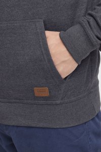 Grå fleece sweatshirt med sidelomme og et brunt lædermærke. Har ribbet manchette og kant, med struktureret stof.