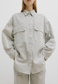 Gestreepte blouse in witte en zwarte katoen, met twee voorzakken en een relaxte pasvorm met verlaagde schouders.