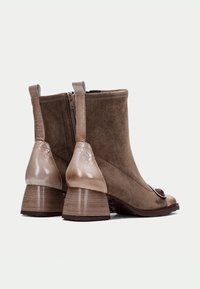 Botas de ante marrón hasta el tobillo con acentos beige brillantes, puntera redonda y un tacón bloque a rayas. Presentan una cremallera en la parte trasera para facilitar su uso.