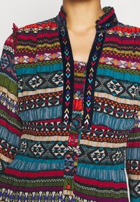 Robe tissée multicolore avec des motifs complexes ; présente un devant boutonné, un col orné et des textures contrastantes dans diverses teintes.