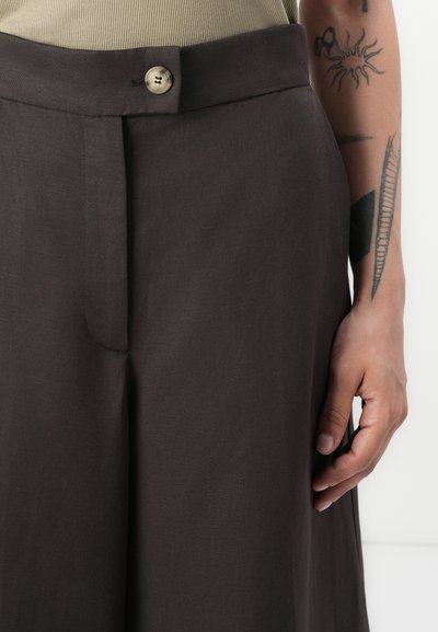 Pantalones de pierna ancha en marrón, fabricados con un tejido ligero y texturizado. Cuentan con un cierre de botón en la cintura y un detalle de pliegue frontal.