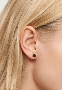 Kvadratisk guldbroschör fäst vid en piercad öra, med en slät yta och polerad finish, som mäter cirka 5 mm.