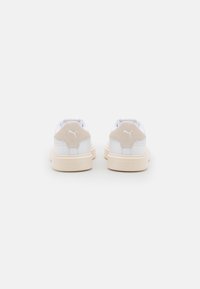 White sneakers with light beige suede accents, a cushioned sole, perforated detailing on the heel, and embossed logo on the back.