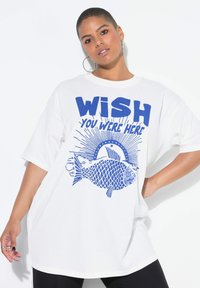 Wit oversized t-shirt met blauwe grafische tekst "WISH YOU WERE HERE" en een visillustratie, met korte mouwen en een ronde hals.