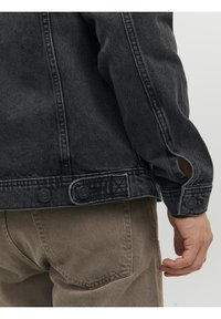 Black denim jacket with light distressing, featuring front buttons, and side slits at sleeves. Neatly stitched with a slightly textured finish.