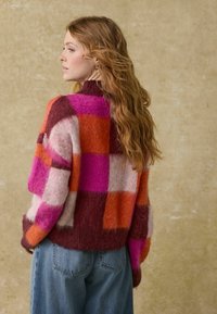 Kolorowy sweter w kratę o oversize'owym kroju w odcieniach różu, pomarańczy i burgundu. Miękka tekstura z wysokim kołnierzem.